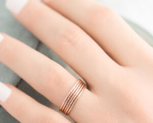  A hand with rose gold diamond-textured stacking rings, against a blurred green velvet backdrop. 
